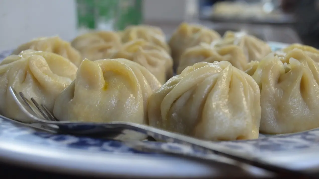 A plate of steamed momos, a popular Nepalese and Tibetan dumpling, with a fork and spoon.