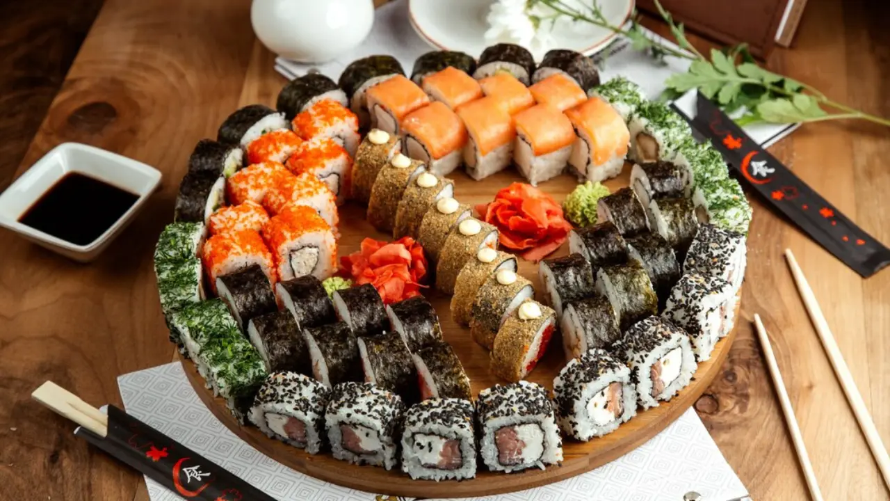 A large wooden platter filled with a variety of colorful sushi rolls, including maki rolls, nigiri, and uramaki.