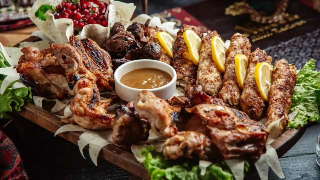 A platter filled with various grilled meats, including skewers, wings, and possibly liver, served with lemon wedges and a dipping sauce.