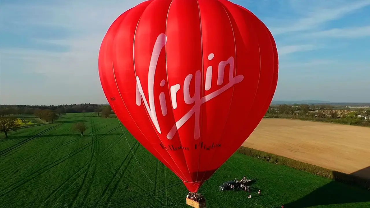 A vibrant red Virgin hot air balloon floating above a picturesque countryside landscape.