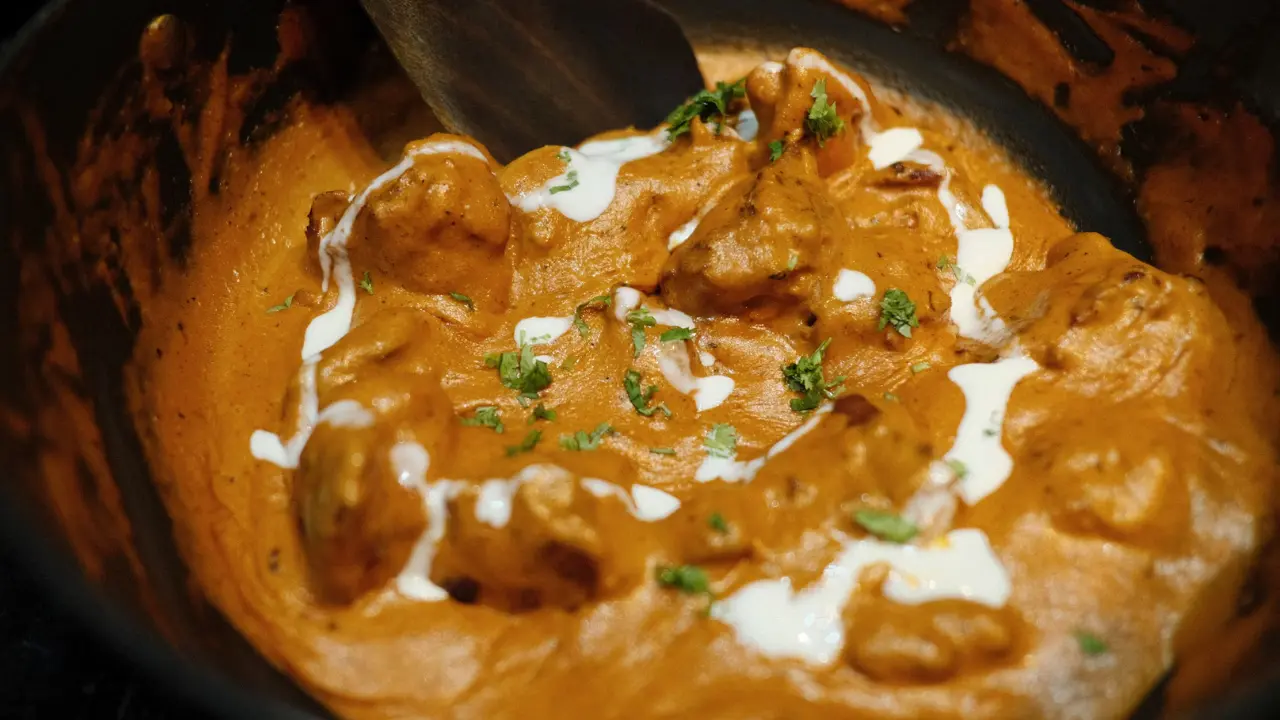 A close-up of a rich, creamy butter chicken dish with chunks of tender chicken in a velvety sauce, garnished with fresh cilantro and dollops of yogurt.