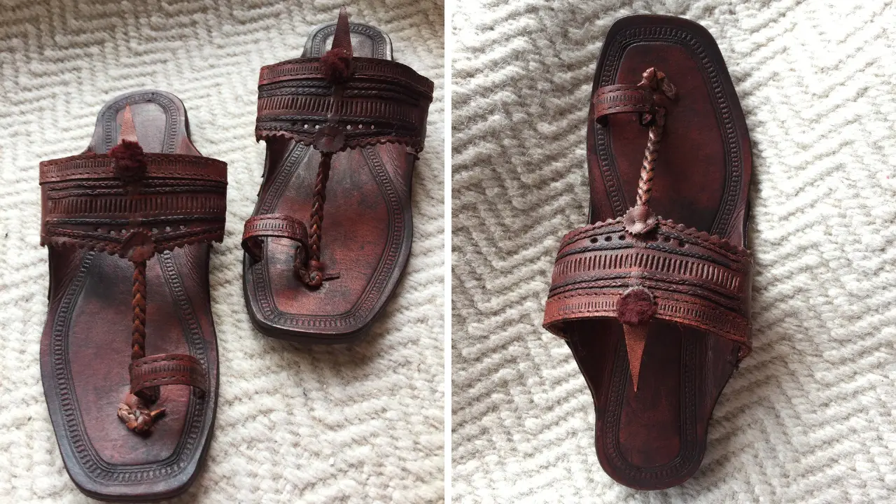 A pair of brown leather Kolhapuri chappals with intricate detailing and a braided strap.