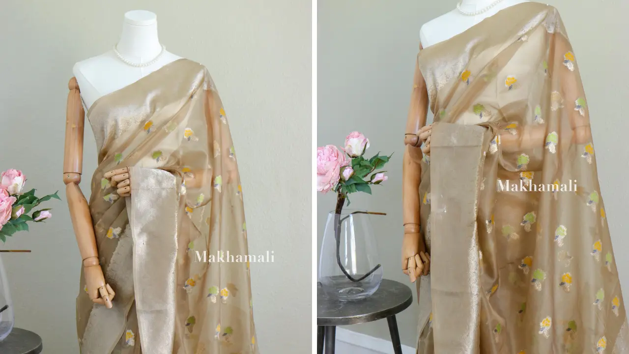 A golden organza saree with delicate floral motifs embroidered on it. The saree is draped on a mannequin and displayed against a white background.