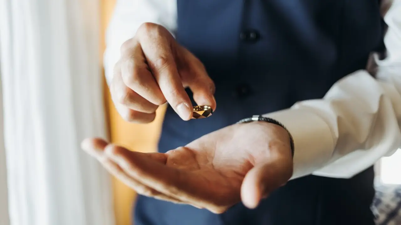 Close-up of a groom's hand holding a gold wedding ring