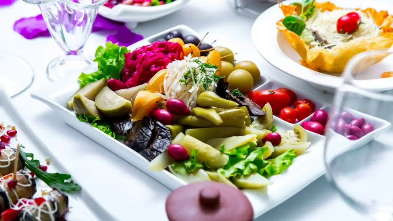 A platter filled with a variety of pickled vegetables, including olives, peppers, tomatoes, and cabbage.