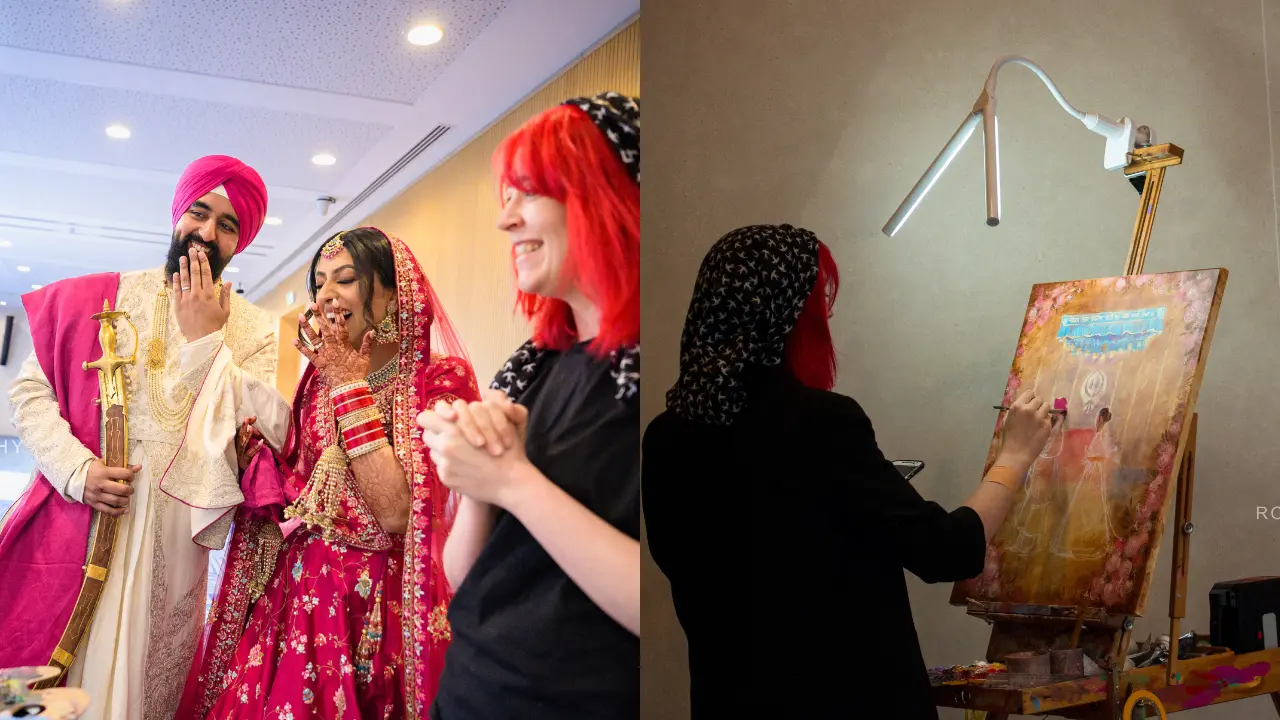 A wedding couple is being painted by an artist at their wedding. The bride is wearing a beautiful red and gold lehenga, while the groom is in a white and pink sherwani. The artist is wearing a black shirt and a black hijab, and is using a brush to paint the couple on a canvas. The painting is in a traditional Indian style, and is full of beautiful colors and details. The couple is laughing and looking at each other with love.