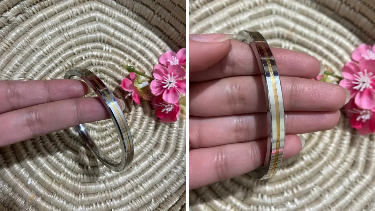 A silver bangle with gold stripes, worn on a person's wrist.