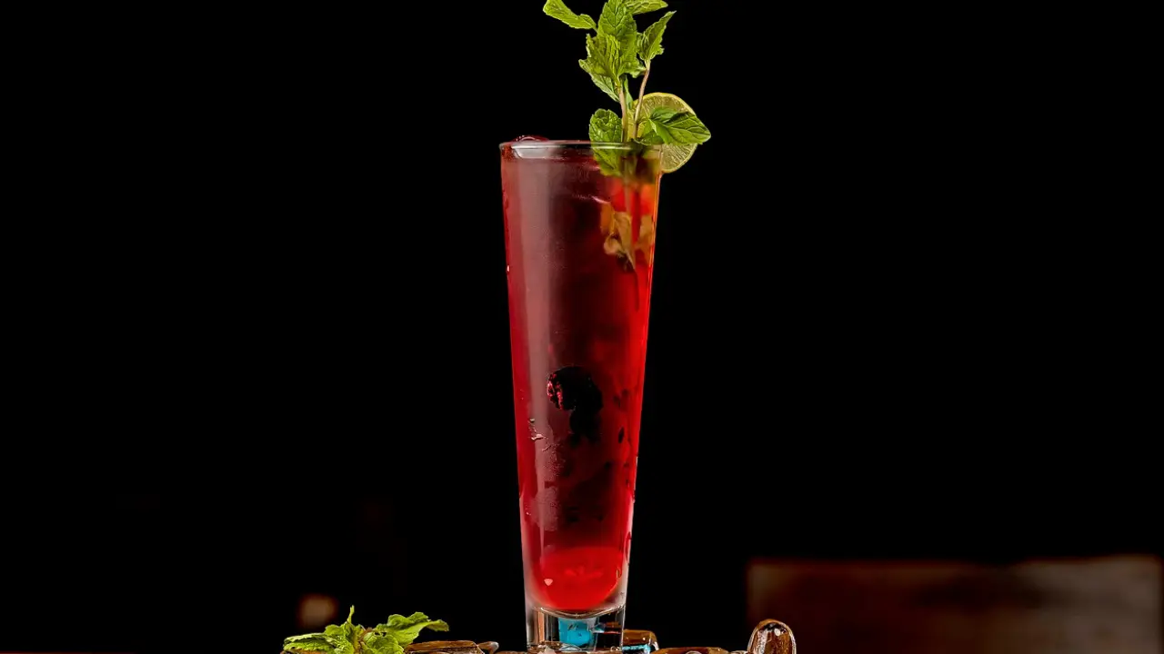 A tall glass filled with a vibrant red cocktail, garnished with fresh mint leaves and a lime wedge.