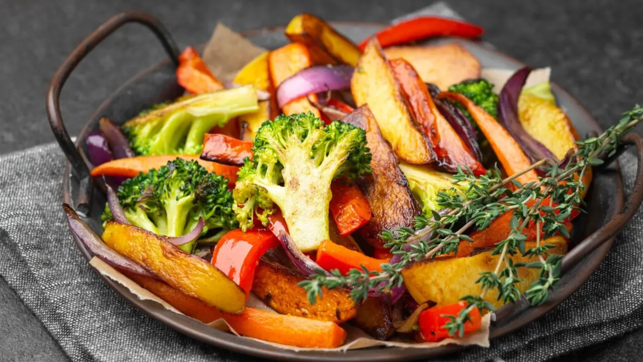 A platter of roasted vegetables, including sweet potatoes, carrots, broccoli, bell peppers, and onions, seasoned with herbs.