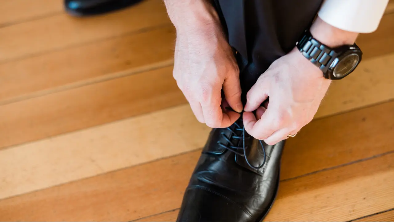 A man tying the laces of a black dress shoe.