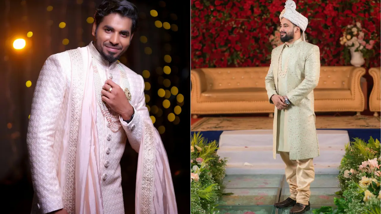 Two men in traditional Indian attire standing in front of a wooden door. The man on the left is wearing a burgundy jacket with gold embroidery, and a yellow turban. The man on the right is wearing a white suit with a red handkerchief in his pocket. They are both smiling.