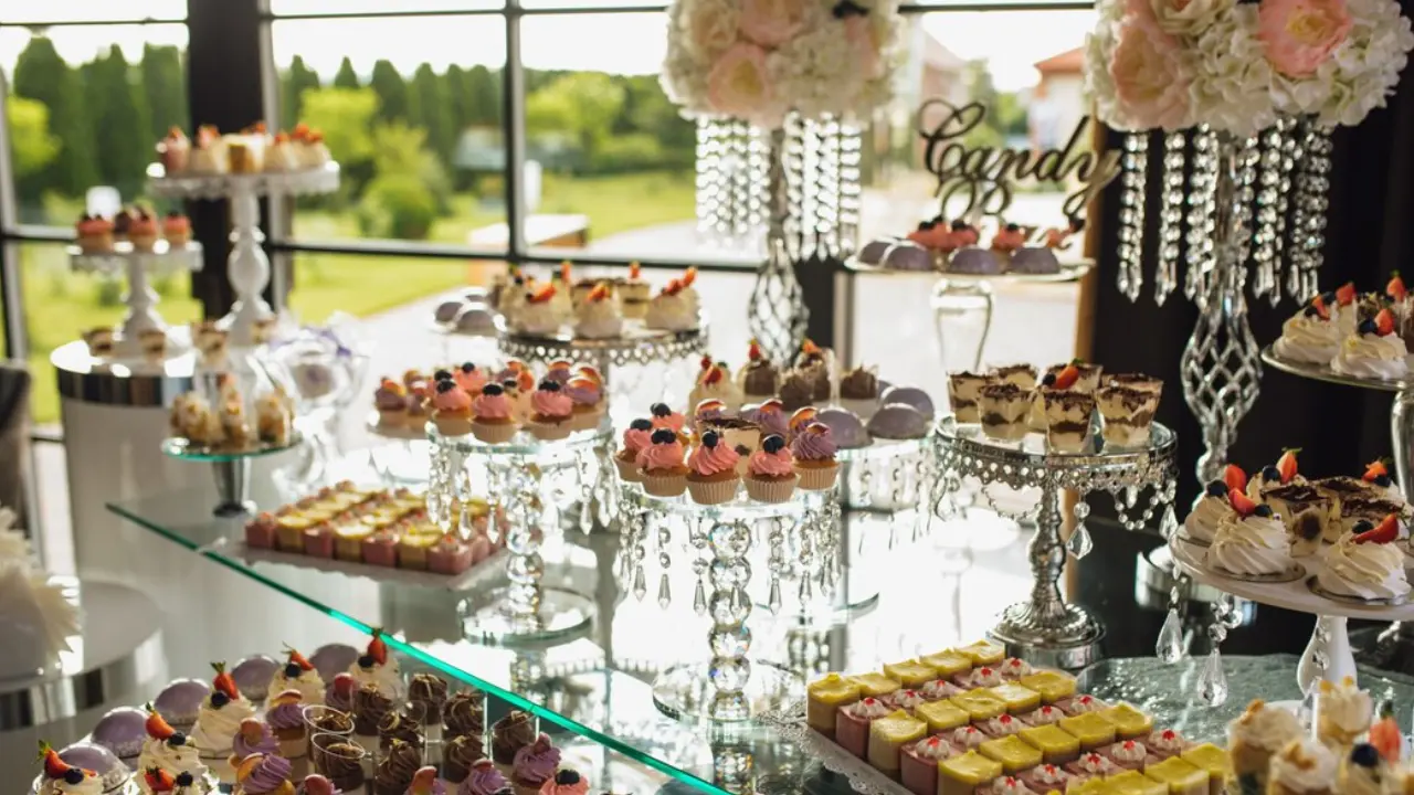 A beautifully decorated candy bar with various desserts, cupcakes, and pastries displayed on glass stands and silver platters.