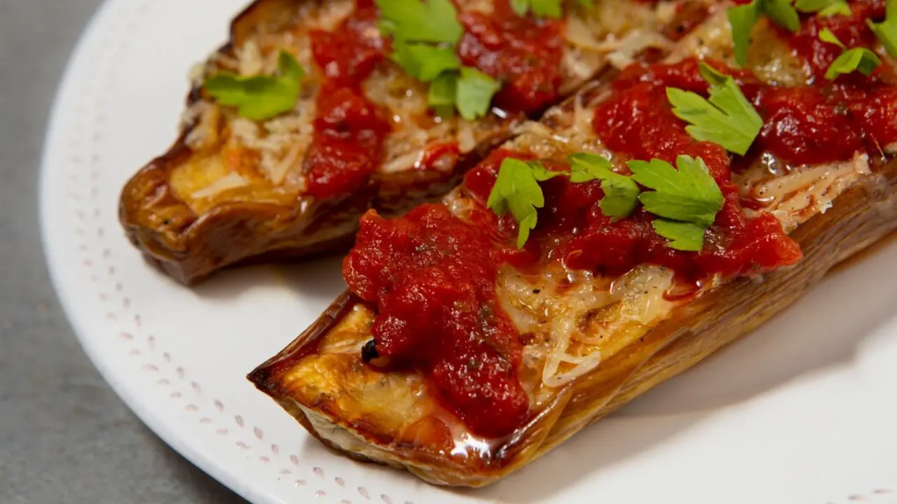 A plate of baked eggplant halves filled with a savory mixture and topped with a rich tomato sauce and fresh parsley.