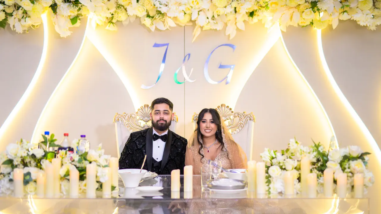 A bride and groom seated at a beautifully decorated wedding reception table with floral arrangements and soft lighting at the National Motorcycle Museum Birmingham.