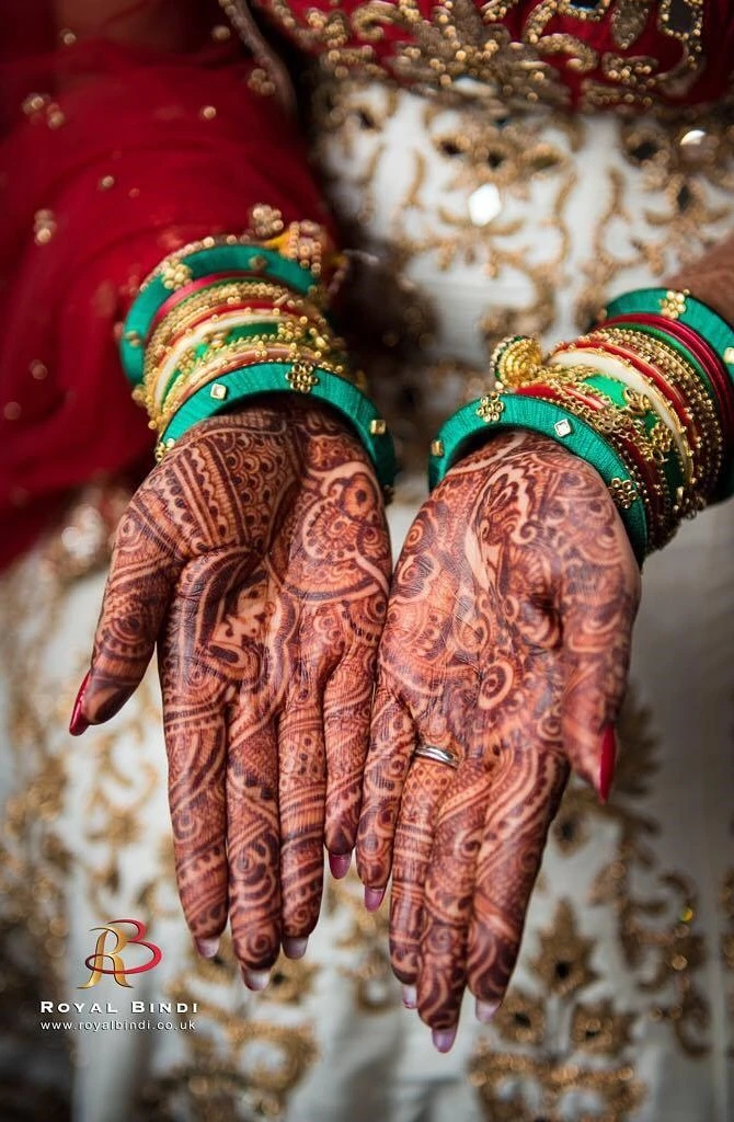 Close-up of intricate henna designs on a bride's hands, with vibrant green and gold bangles.